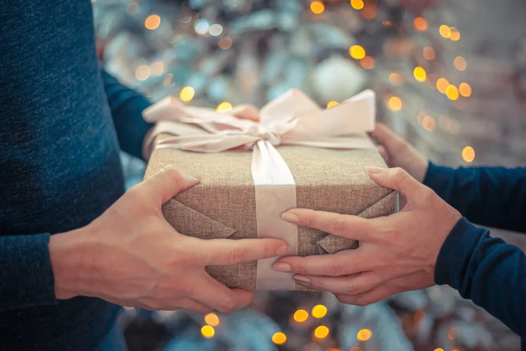 In the picture, a close-up of the hands of two people who are exchanging a gift.
