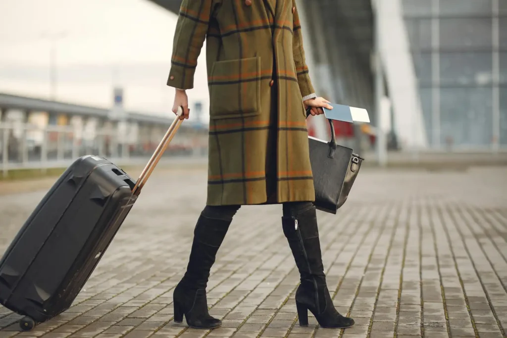 In the picture, a close-up on the legs of a woman dragging a trolley. In the other hand she holds a bag and a passport.
